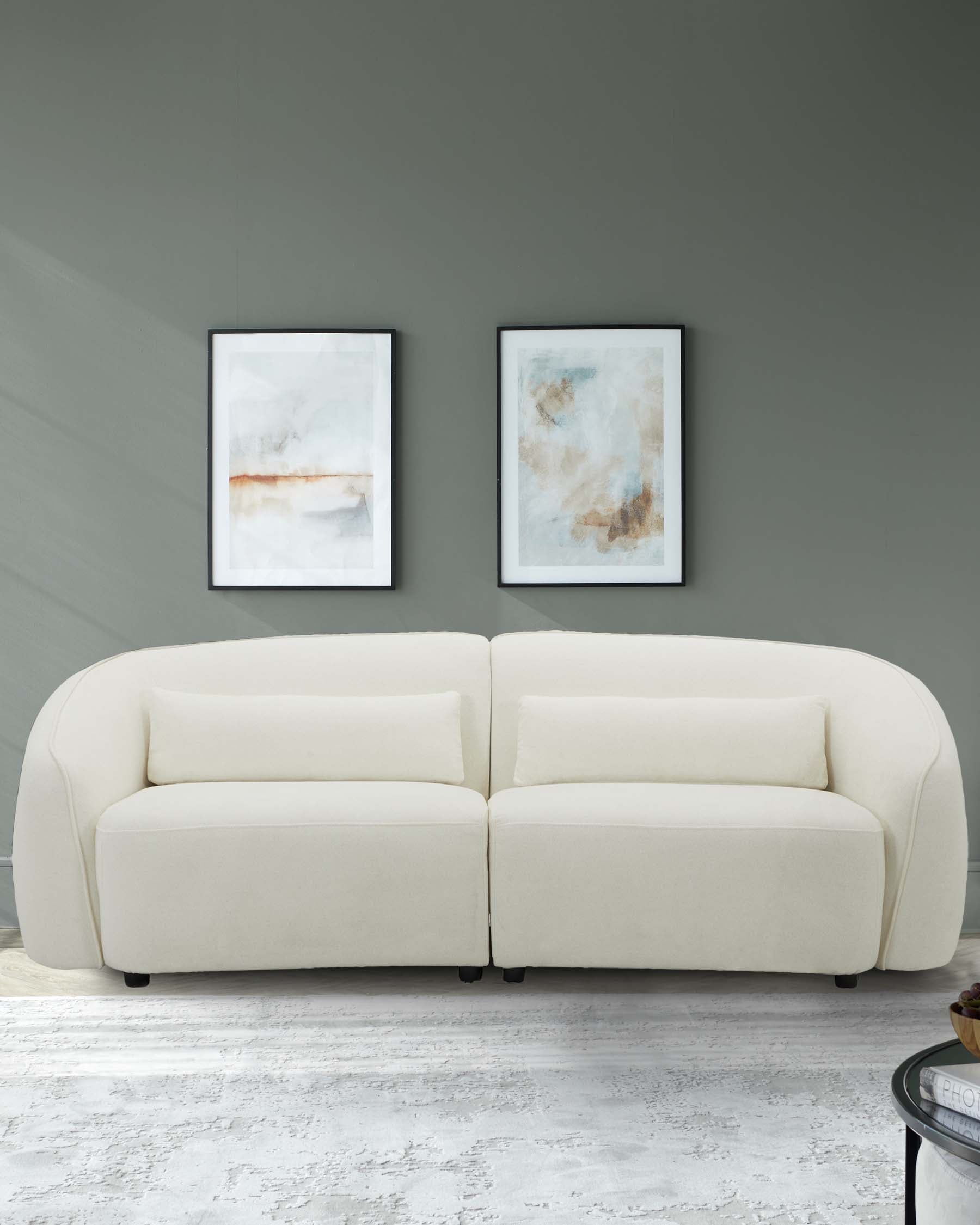 Curved white sofa with two back cushions, paired with minimalist framed artwork on a neutral wall, creating a modern aesthetic.