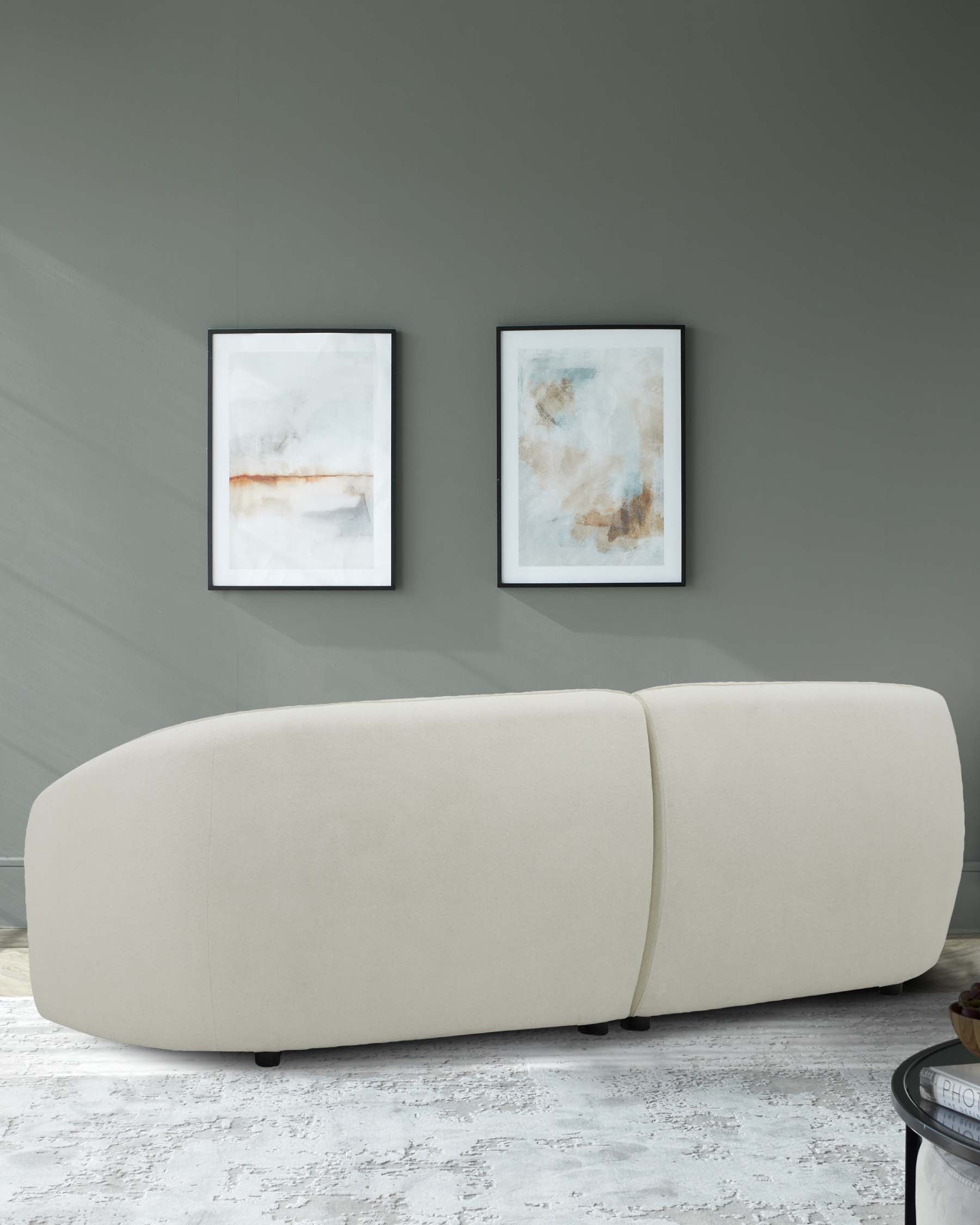 A modern, curved beige sofa with minimalist design, complemented by two abstract framed art pieces on the wall.