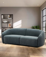 Curved, soft teal sofa with plush upholstery, paired with a modern black shelving unit and a touch of greenery.