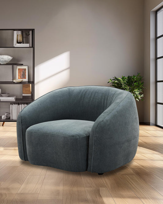 Curved, plush teal armchair with a wide seat, set on a warm wooden floor, creating a cozy and modern living space.