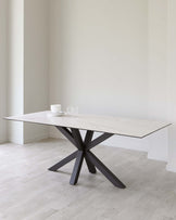 Modern minimalist dining table with a white marble top and a striking black angular metal base, set in a room with light wood flooring and neutral walls.