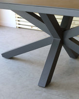 Modern grey dining table with a solid rectangular top and a distinctive geometric base composed of intersecting angular supports.