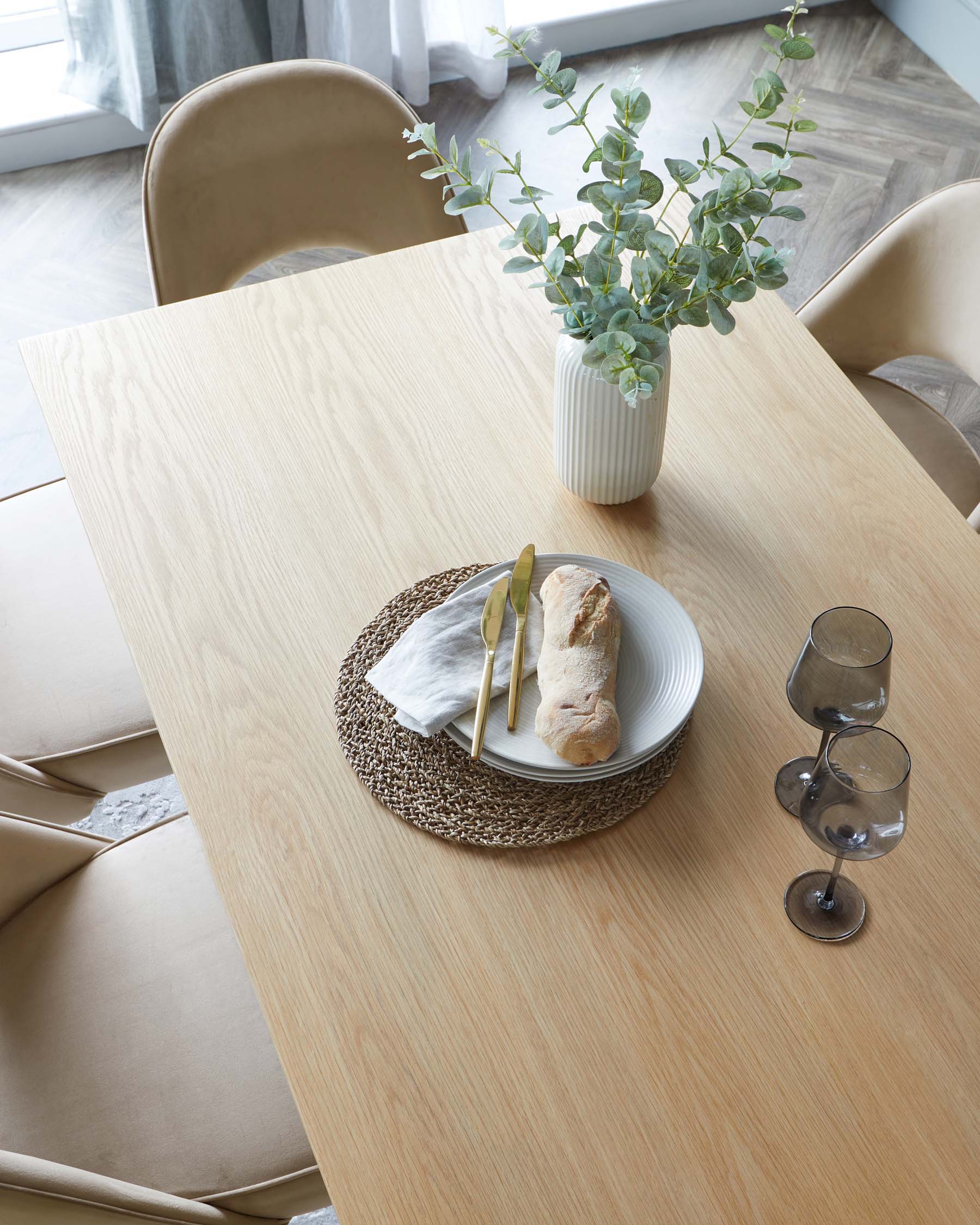 A modern dining area featuring a rectangular wooden table with a light finish. Surrounding the table are curved, beige upholstered chairs with a sleek, minimalist design.