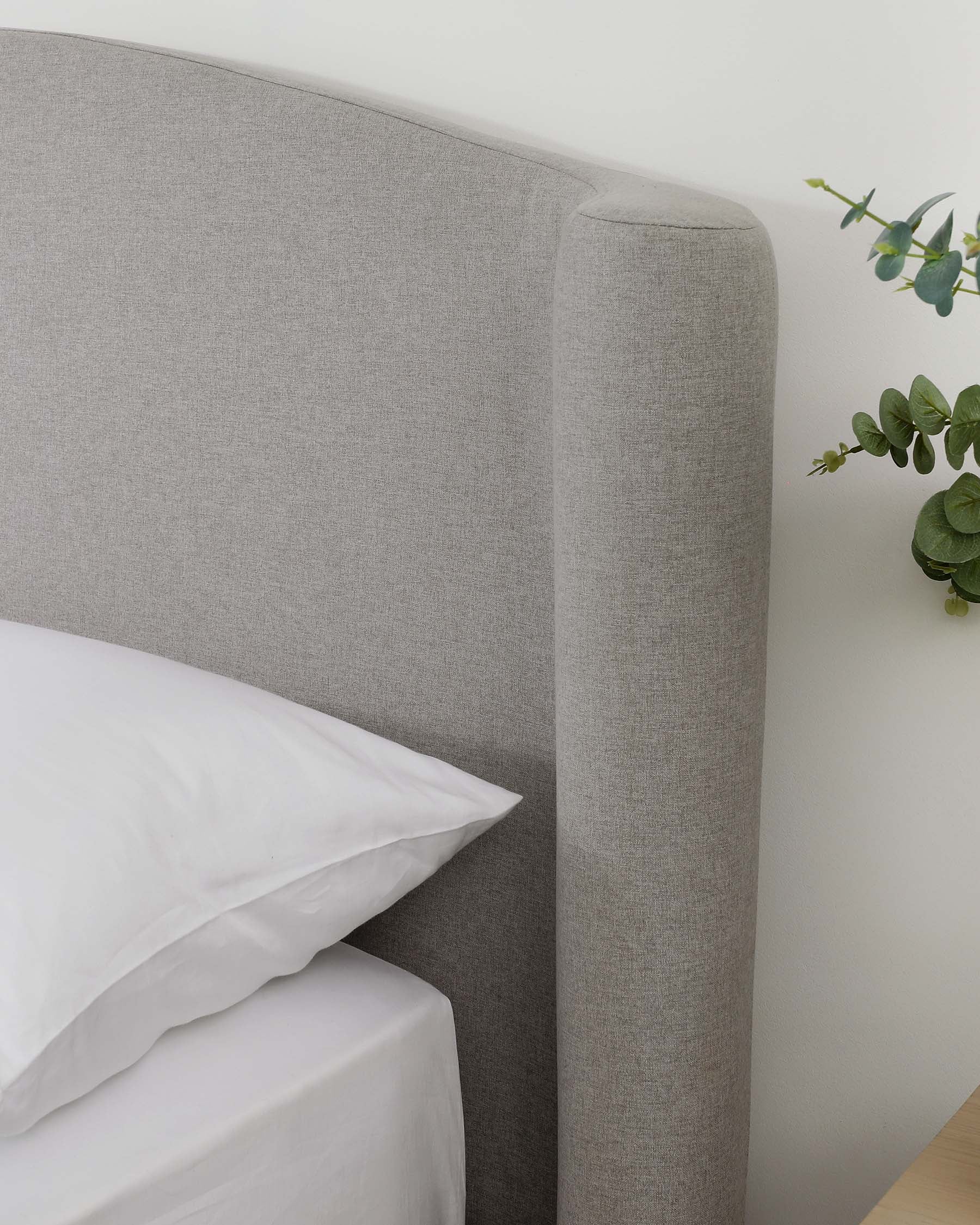 Modern grey upholstered headboard with a rounded edge design, displayed as part of a simplistic and elegant bedroom setup.