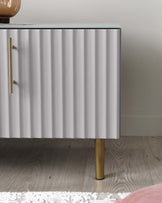 Modern fluted cabinet in a white finish with brass cylindrical legs and hardware.