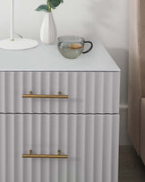 Modern white chest of drawers with sculpted, wave-like front panels and brass horizontal handles, displaying a minimalist aesthetic.