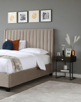 Elegant bedroom scene featuring a contemporary, beige, upholstered bed with a tall, tufted headboard and a simple black bedside table with a sleek design, complemented by a soft white and beige bedding set.