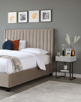 Upholstered king-size platform bed with a tall, button-tufted headboard in a neutral taupe fabric. Beside the bed, a contemporary grey concrete-effect side table with a black metal frame, featuring a lower shelf and tabletop accessories.