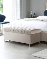 Elegant light grey upholstered bench with a plush, tufted top cushion, featuring a streamlined design and metallic legs, positioned at the foot of a bed in a modern bedroom setting.