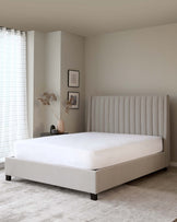 Modern minimalist style bedroom with a large beige upholstered bed featuring a vertical channel-tufted headboard and a coordinating platform base, set on a textured grey area rug.