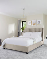 Elegant upholstered king-size bed with a high tufted headboard in a neutral colour, two white modern bedside tables with drawers, and a matching beige bedroom bench at the foot of the bed. The bed is dressed in white linens with a textured throw at the end.