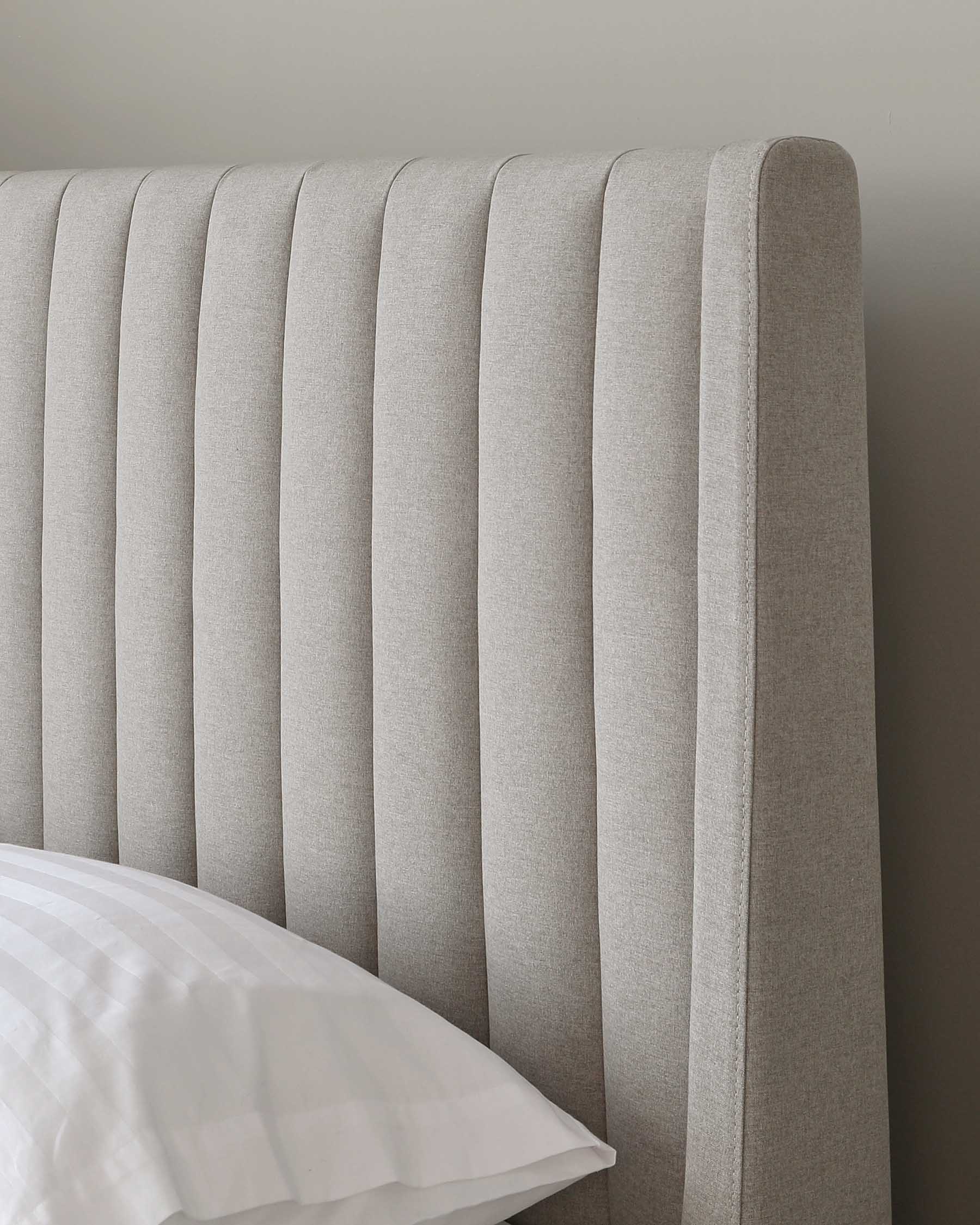 A modern upholstered headboard in light grey fabric with vertical channel tufting, partially obscured by a corner of a white bedsheet.