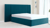 A modern teal upholstered king-size platform bed with a tall, vertically channelled headboard and a minimalist frame that sits flush with the mattress, set against a light and airy bedroom interior.