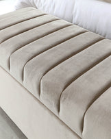 Close-up of a contemporary beige upholstered bench with channel tufting.