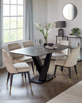 Elegant dining room featuring a modern dark wooden table with a geometric base in matte black, complemented by a set of four plush beige chairs accented with quilted detailing and black legs tipped with gold. A minimalist dark side table with a round mirror above it, a stylish table lamp, a small pile of books, and an arrangement of plants complete the scene.