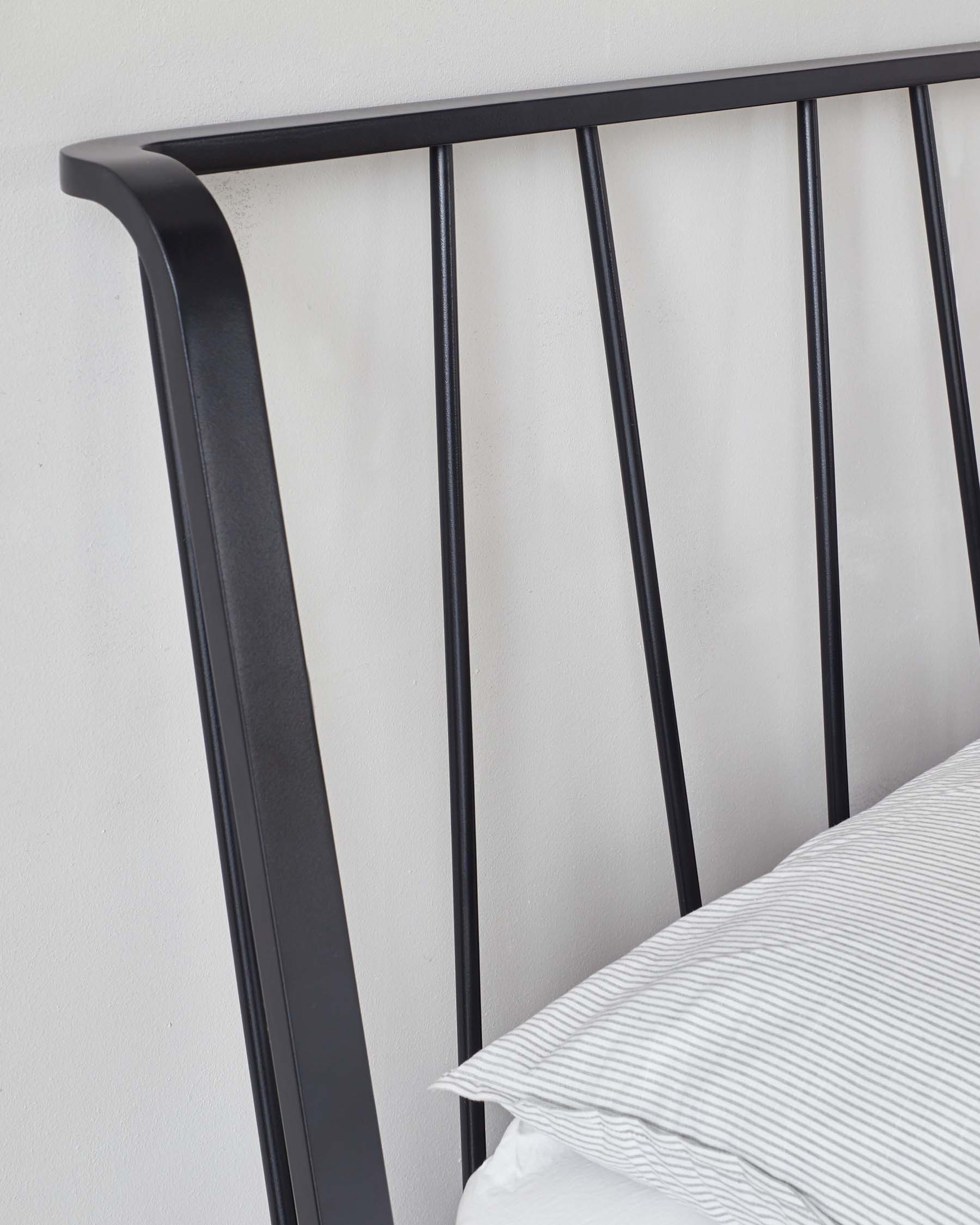 Contemporary black metal headboard featuring vertical bars and a curved top rail, partially shown with a striped pillow and a hint of a bed.