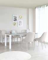 A modern dining room featuring a simple white rectangular dining table paired with four beige upholstered chairs with a minimalist design. A round, off-white area rug lies on the light wooden floor, complementing the neutral palette of the room.