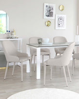 Modern minimalist dining set featuring a white rectangular table with a glass top and sleek metal legs, accompanied by four upholstered chairs in light grey fabric with slender, tapered legs in a matching white finish. A white console table with decorations stands against the wall in the background.