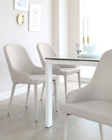 Modern minimalist dining room set featuring a clean-lined white table with a sleek grey tabletop and a set of stylish matching white upholstered chairs with gently curved backrests for comfort. The set stands on light hardwood flooring, enhancing the room’s bright and airy aesthetic.