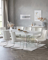 Modern dining room featuring a sleek white rectangular table with a high-gloss finish and reflective chrome legs, accompanied by six white leather upholstered chairs with curved chrome bases. A white textured rug underlays the set, and the scene is completed with a contemporary chandelier overhead.