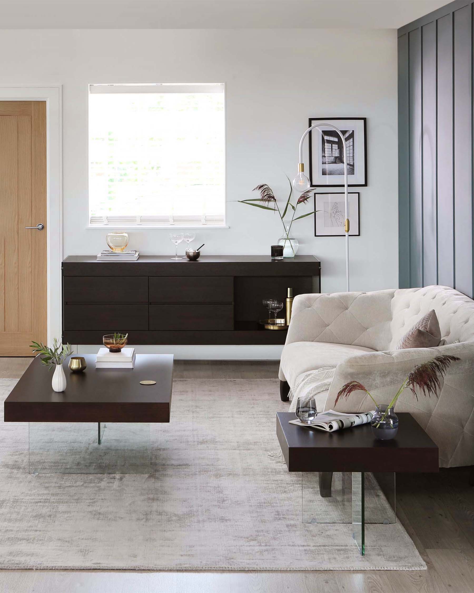 Contemporary living room furniture including a dark brown wooden sideboard with sleek metal handles, a tufted off-white fabric sofa, and two modern rectangular coffee tables in a dark finish with glass legs.