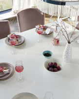 Modern dining set with a white oval table and four taupe upholstered chairs with high, curved backs.