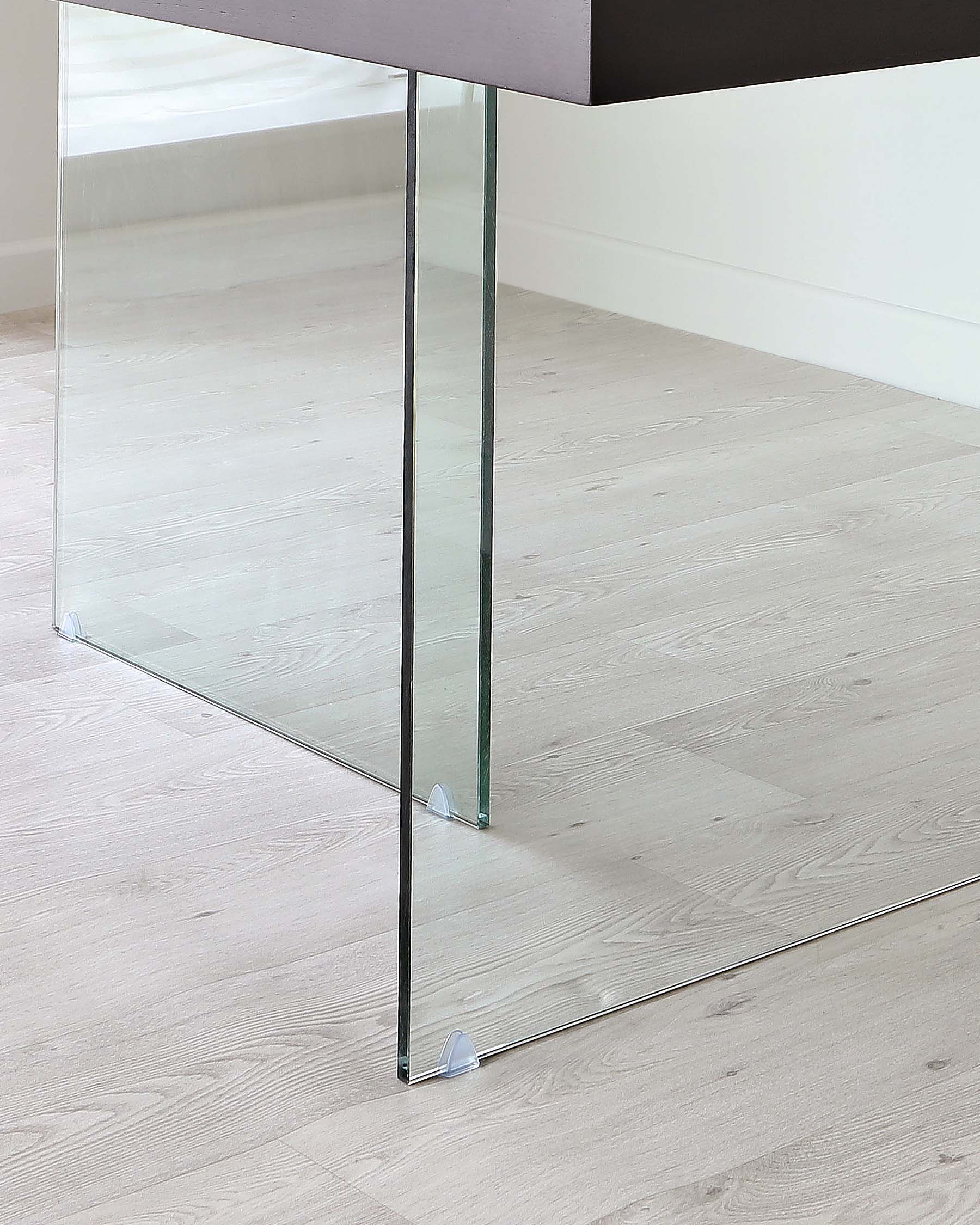 Modern glass table leg with a sleek chrome finish, providing a clear view to a light hardwood floor through its transparent structure.