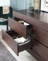 A contemporary wooden sideboard with a dark brown finish, featuring multiple drawers with circular black metal pulls. Two drawers are open, revealing items inside for decorative staging: one with neatly arranged cutlery and the other with stylish linens. The sideboard's surface displays a selection of decorative items such as vases and a glass, enhancing the modern aesthetic of the piece.