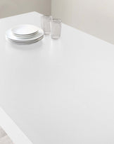 A modern minimalist white dining table with a smooth top and clean lines, set against a neutral background.