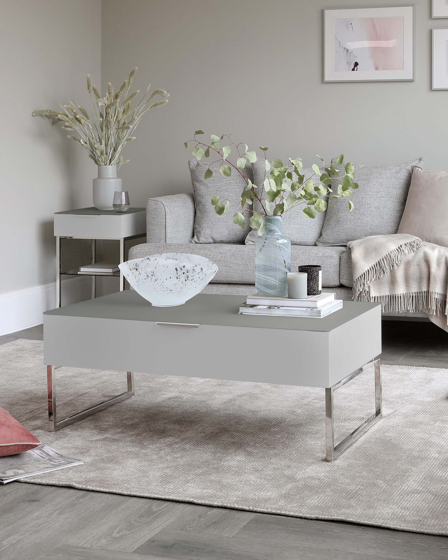 A modern living room featuring a sleek, light grey upholstered sofa complemented by a grey rectangular coffee table with a smooth finish and metallic accents. Beside the sofa is a matching grey side table with a minimalist design, displaying a simple white vase. The furniture is set upon a textured grey area rug, presenting a harmonious and contemporary aesthetic.