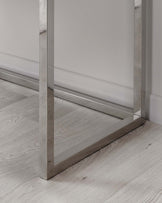 Polished chrome furniture leg with a sleek, square profile, supporting a structure out of view, on a light wood laminate flooring.