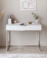 Modern minimalist white desk with sleek chrome legs, featuring a clean tabletop with an elegant, slender silhouette ideal for contemporary interiors.