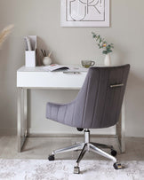 Modern minimalist home office setup featuring a sleek white desk with metal legs and a stylish grey upholstered office chair with a high back, horizontal stitching details, and a chrome swivel base with casters.