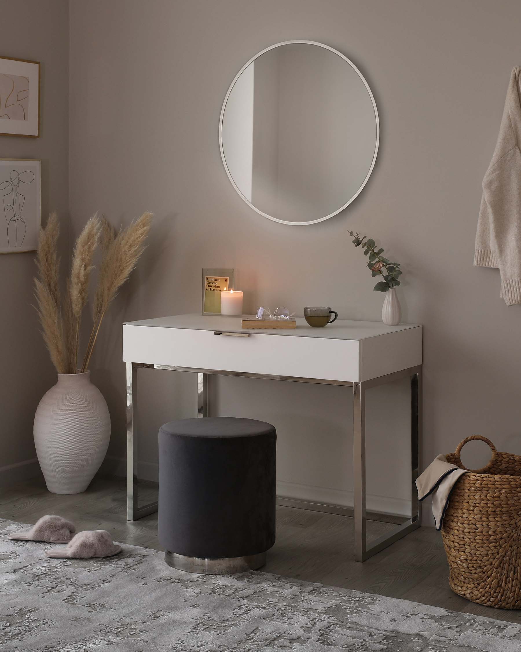 Modern minimalist furniture set consisting of a clean-lined white console table with a drawer and slim metal legs, paired with a round, upholstered dark-coloured stool with a metallic base. The set is complemented by a large round wall mirror above the table.