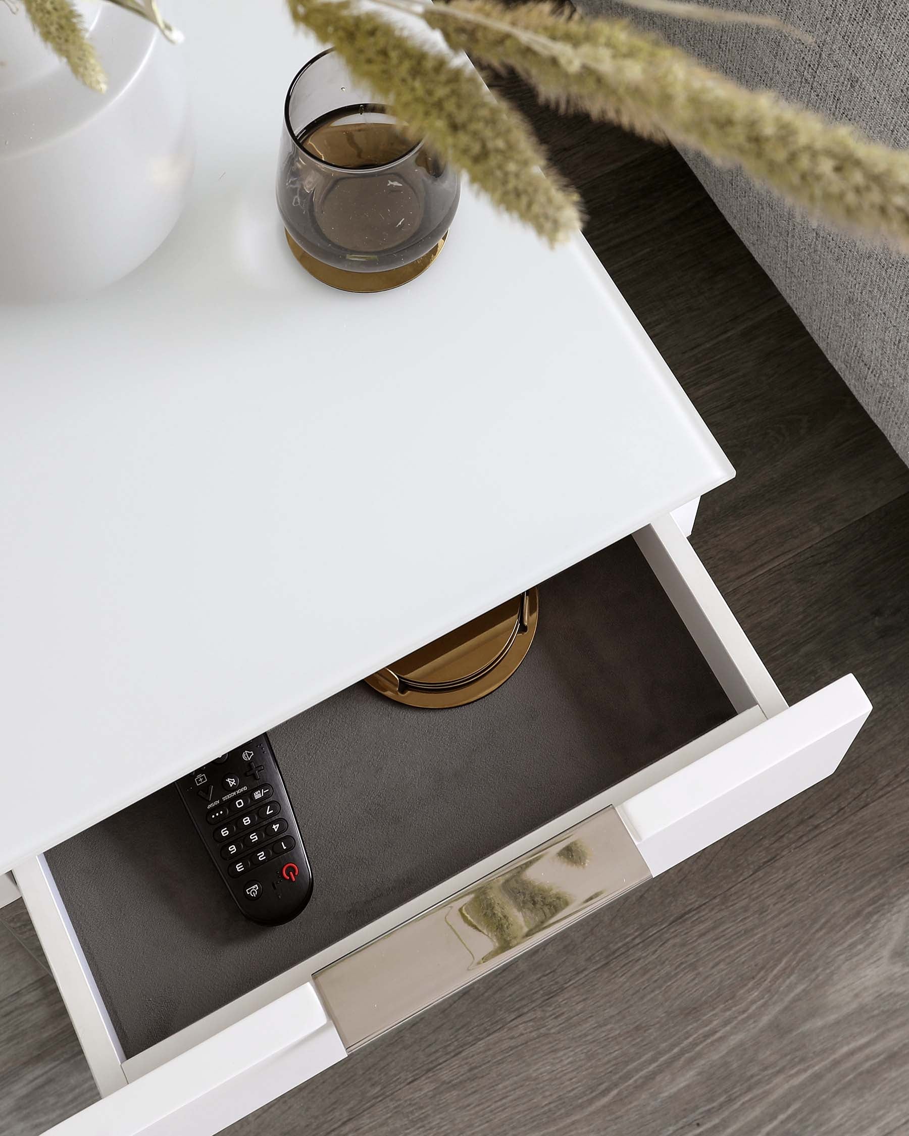 White modern bedside table with an open drawer, featuring neat storage for remote controls and accessories, a sleek handle, and a reflective base accent.