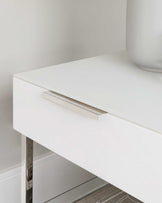 Modern minimalist white drawer with sleek silver handle and stainless steel legs.