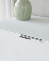 Modern minimalist white drawer with a sleek metal handle, complemented by a textured green ceramic vase atop its smooth surface.