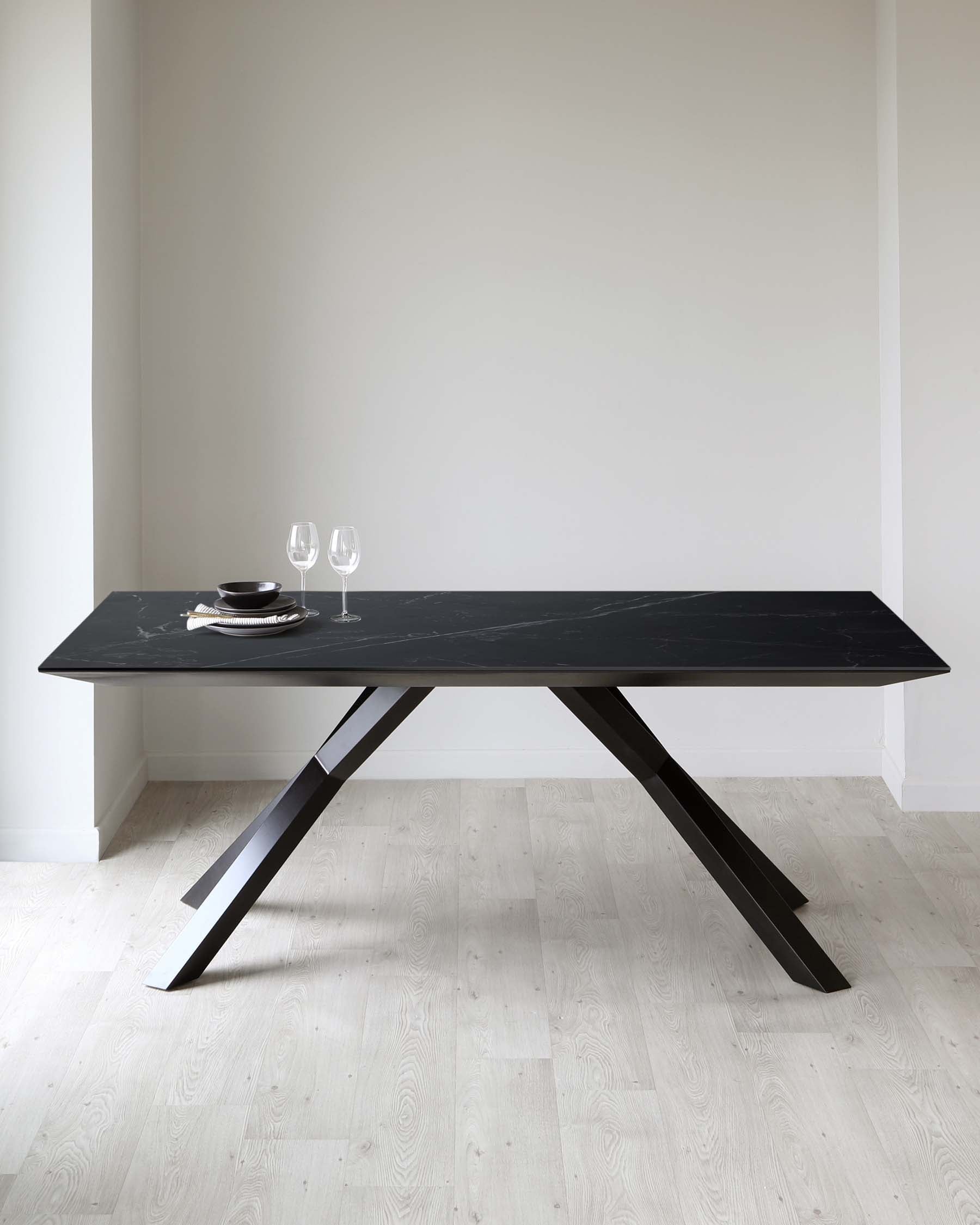 Modern rectangular dining table with a black marble tabletop and angular black metal legs. Table set with minimalistic dinnerware and two wine glasses.