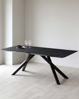 Modern rectangular dining table with a sleek black marble top and angular black metal legs, staged with simple dinnerware and wine glasses, set against a neutral backdrop and light wooden flooring.