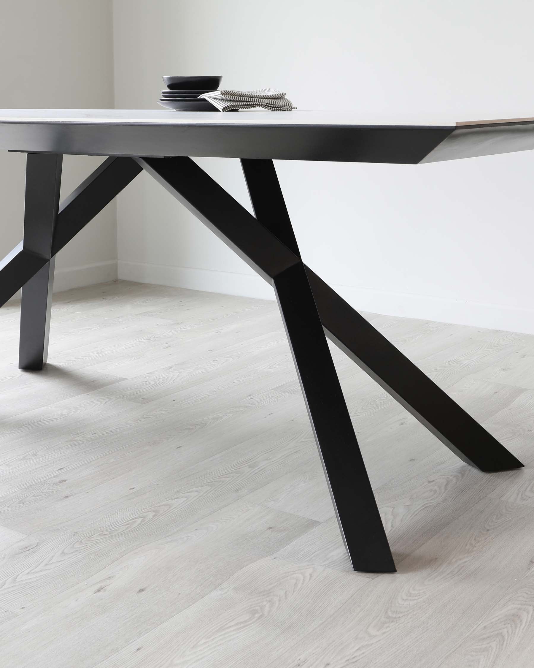 Modern minimalist black dining table with a sleek tabletop and angular legs, accompanied by simple decorative black bowls and books on top, set against a neutral background.