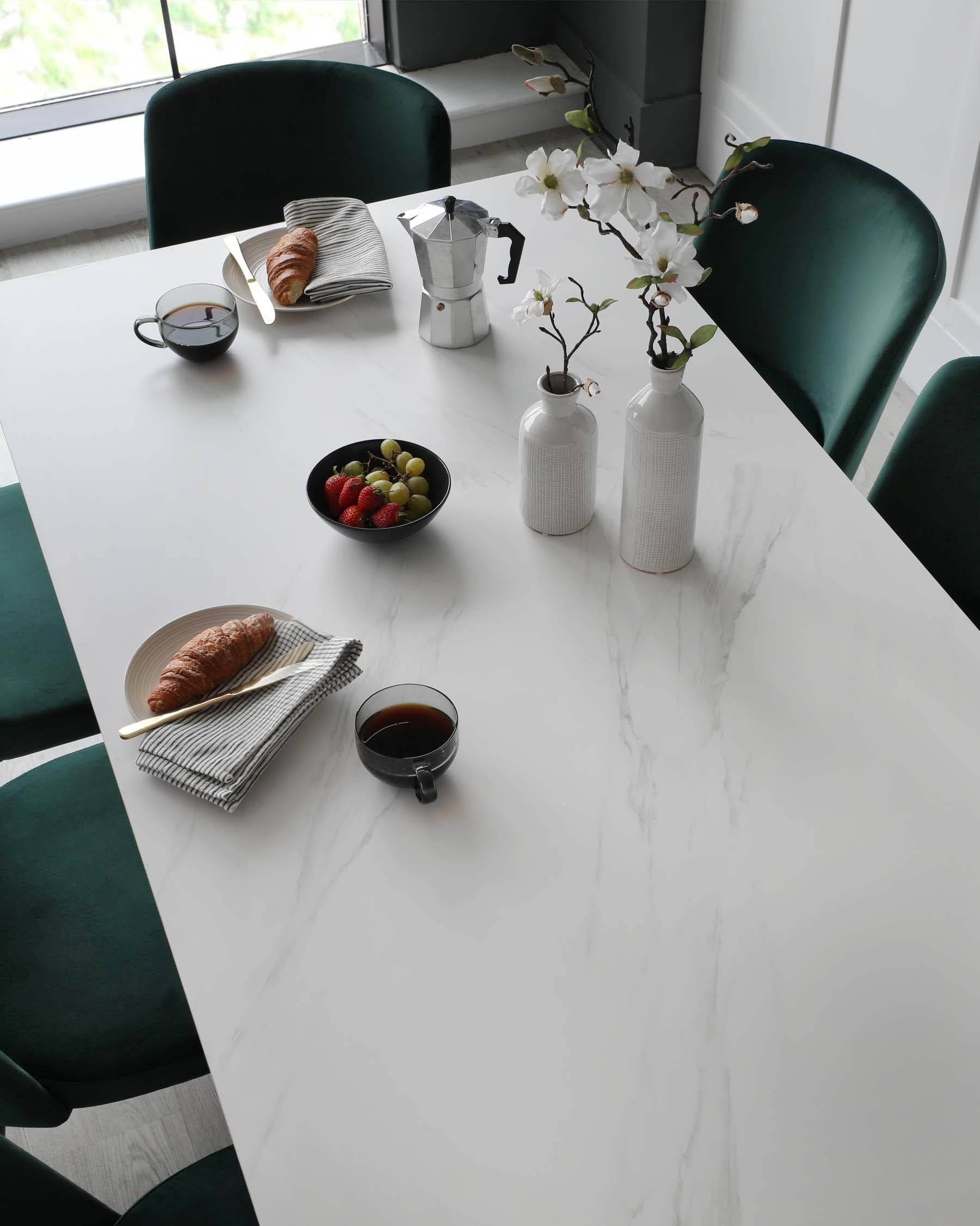 Modern dining space featuring an elegant marble-top table with a sleek white surface and subtle vein detailing. Paired with plush, forest green upholstered dining chairs with a smooth, velvet texture and rounded backs, offering sophistication and comfort.