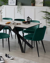 Modern dining set featuring a white marble-top table with black angular legs, accompanied by four plush velvet chairs in a rich emerald green with sleek black legs. The set communicates a blend of contemporary style and comfortable dining experience.