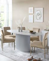 Modern dining room with an oval white table featuring a fluted pedestal base, surrounded by four beige upholstered chairs with slender metal legs, set on a textured white area rug.