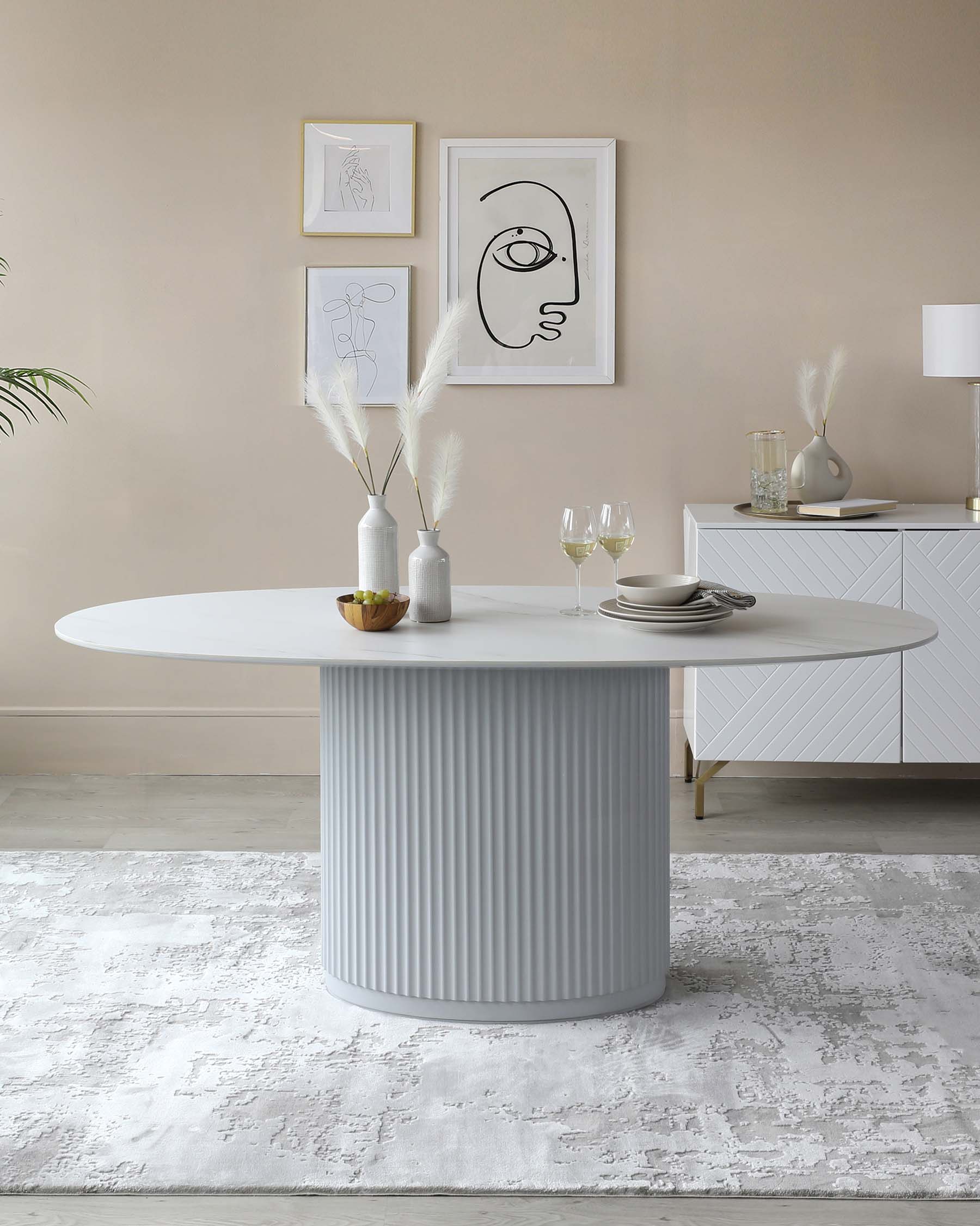 Contemporary oval dining table with a fluted cylindrical base finished in a pale grey colour, paired with a sleek sideboard featuring line-patterned facade details in the background.