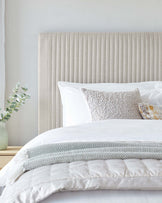 Elegant modern bedroom featuring a neutral-toned, vertically channelled headboard with a plush texture, complemented by crisp white bedding accessorized with a mix of textured and patterned decorative pillows.