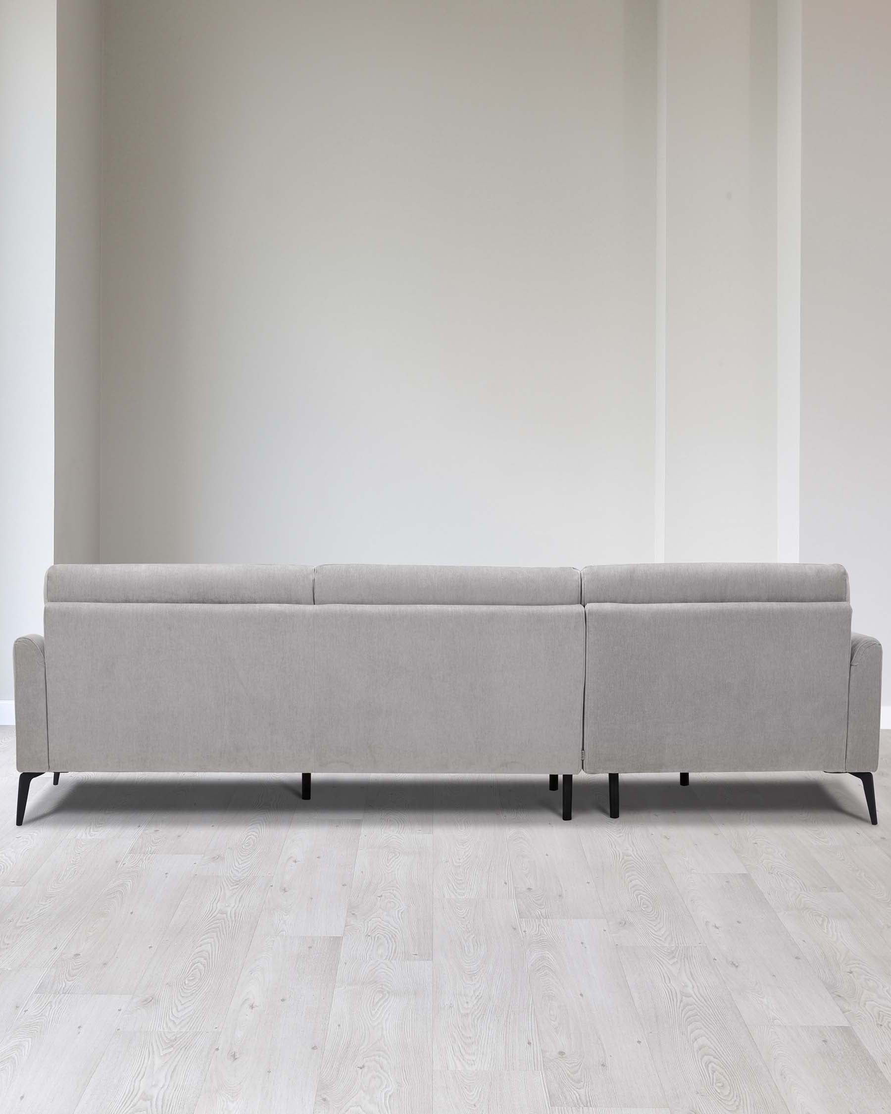 Modern light grey fabric sofa with clean lines and simplistic design, featuring low-profile backrest and cushions, elevated on slender dark legs, shown against a neutral backdrop and light wood flooring.