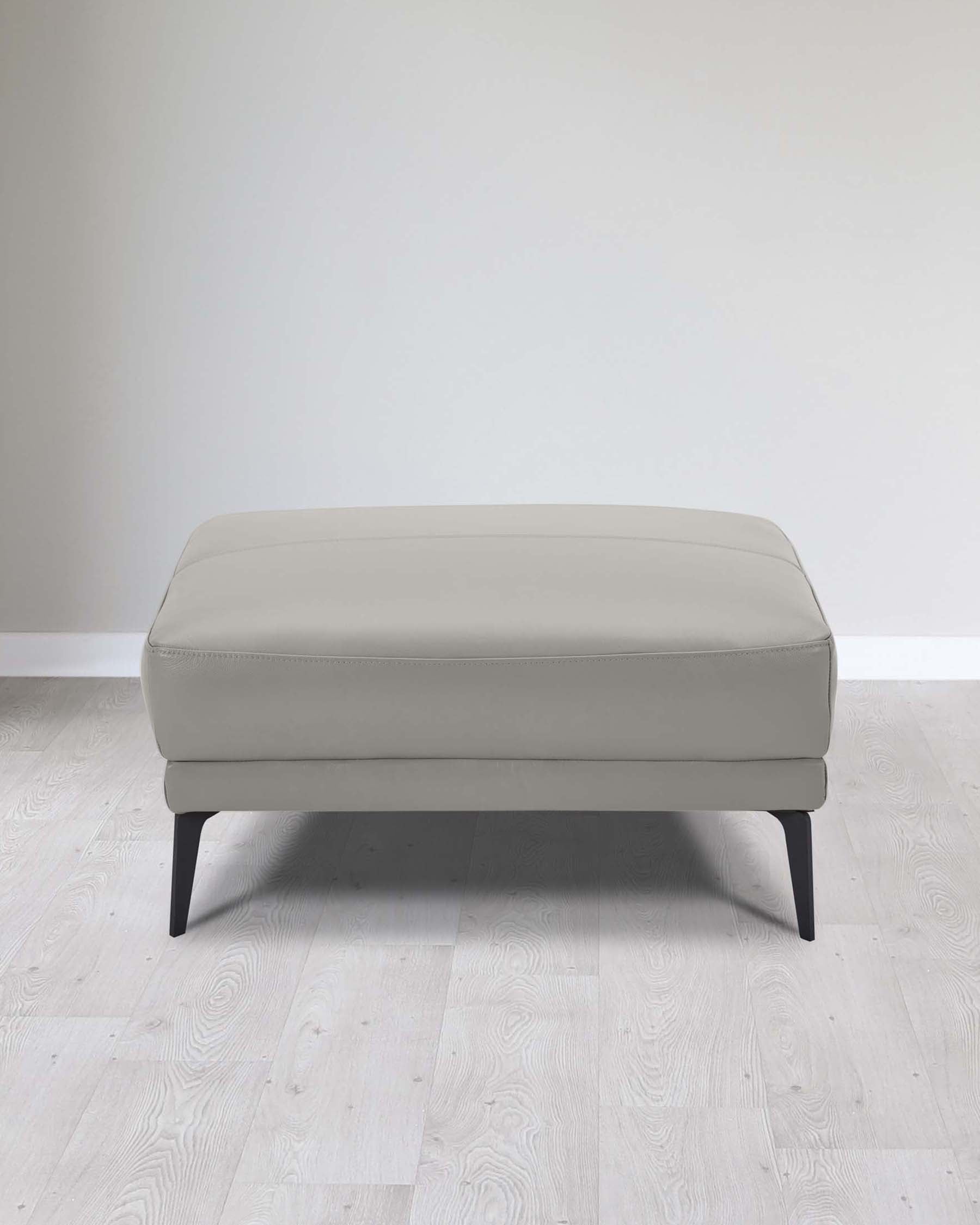 Modern light grey upholstered ottoman with clean lines, featuring a rectangular cushioned top and four dark tapered wooden legs, set against a neutral backdrop with light wooden flooring.