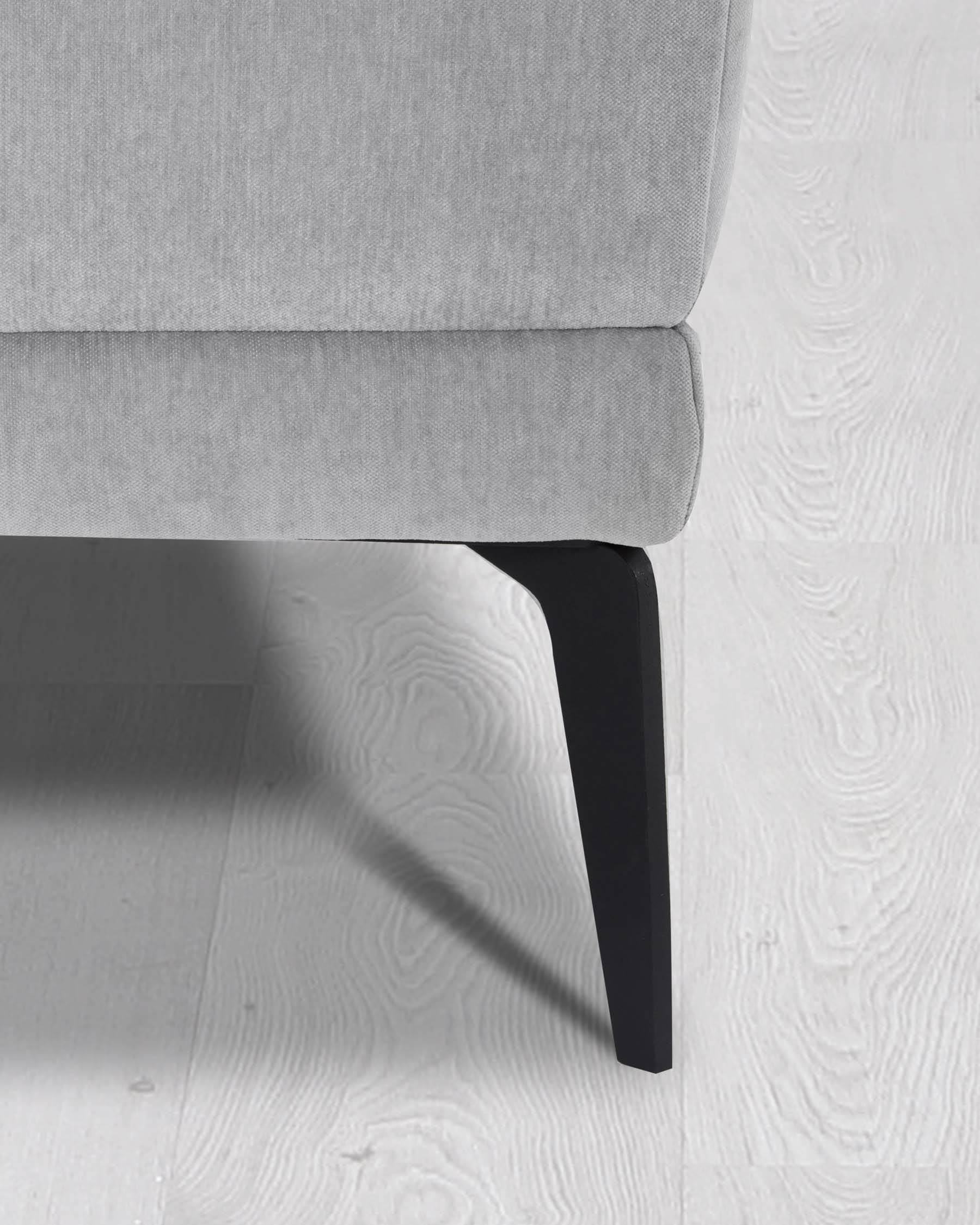 Modern minimalist light grey armchair with sleek black wooden legs on a white textured floor.