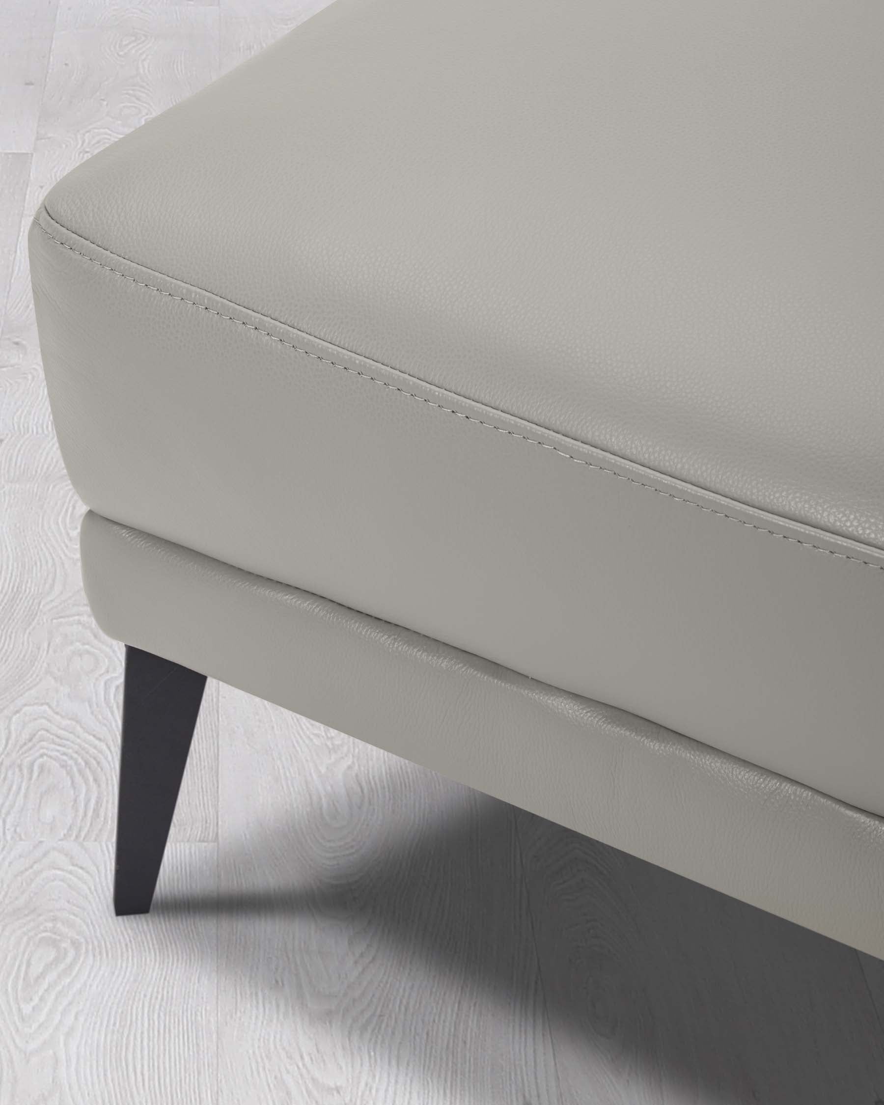 Modern light grey upholstered ottoman with visible stitching detail and dark wooden legs on a white wooden floor.