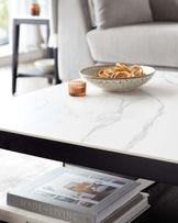 Elegant modern furniture including a marble top coffee table with a dark wooden base and a side table with a minimalist black metal frame and light wooden shelf, complementing a grey upholstered sofa in the background.